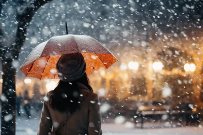 Woman Standing Under Orange Umbrella During Heavy Snowfall