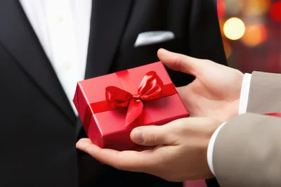 Person Handing A Red Gift Box To Another