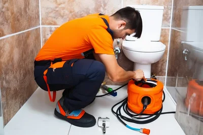 Professional Plumber Using Drain Cleaning Machine In Bathroom