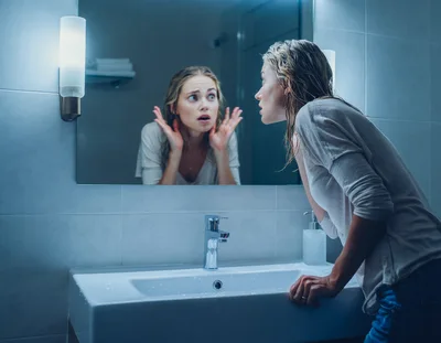 Stressed Woman Looking At Her Reflection In Bathroom Mirror