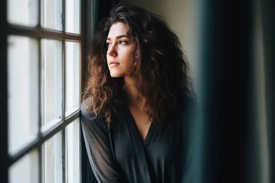 Pensive Young Woman With Curly Hair Looking Out Window