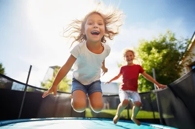 Happy Children Jumping Together On A Backyard Trampoline