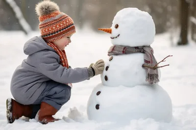 Young Child Building A Snowman In A Snowy Park