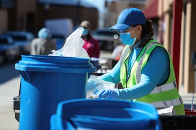 Volunteer Sorting Food Donations Into Blue Bins