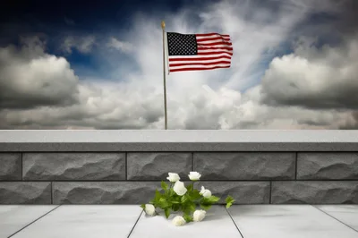 White Roses Placed Before A Stone Wall With American Flag