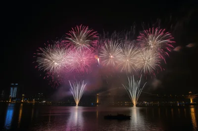 Vibrant Fireworks Display Over A River At Night