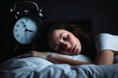 Young Woman Sleeping Peacefully Beside An Alarm Clock