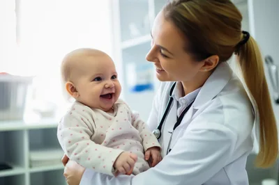 Female Pediatrician Holding A Smiling Baby In Clinic