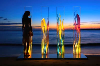 Woman Standing Beside Illuminated Glass Sculptures At Sunset