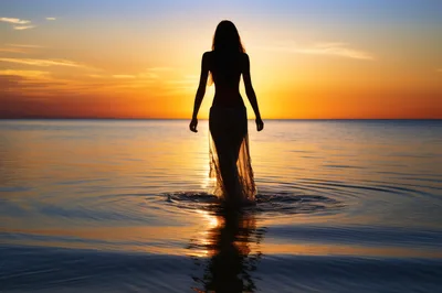 Silhouette Of A Woman Walking In The Ocean At Sunset