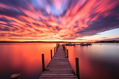 Wooden Pier Extending Into Calm Lake At Sunset