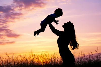 Mother Lifting Her Baby Against A Sunset Sky