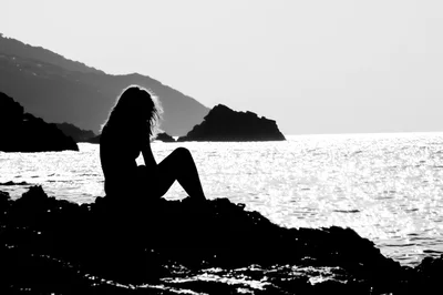 Silhouette Of A Woman Sitting On Coastal Rocks