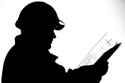 Silhouette Of A Construction Worker Examining Blueprints
