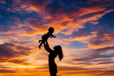 Mother Lifting Her Child Against A Vibrant Sunset
