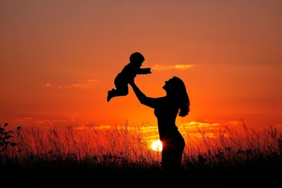 Mother Lifting Her Baby Against A Vibrant Sunset