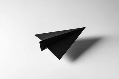 Black Paper Airplane Flying Against A White Background