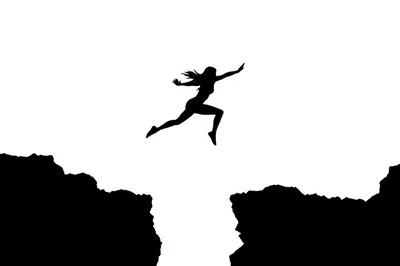 Silhouette Of A Woman Jumping Across A Cliff Gap