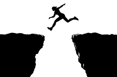 Silhouette Of A Person Jumping Across A Cliff Gap