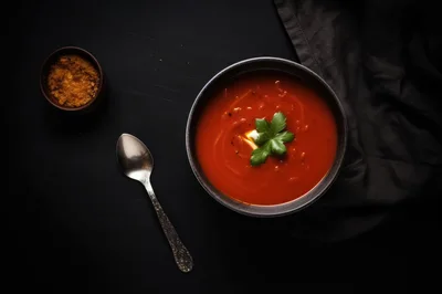 Bowl Of Tomato Soup With Garnish On Dark Table