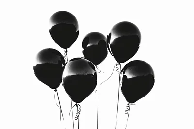 Group Of Shiny Black Balloons Floating Against White Background