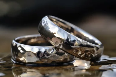 Two Hammered Silver Wedding Bands Resting On Wet Surface