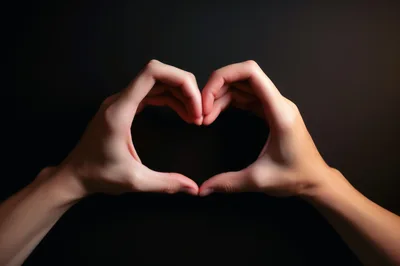Hands Forming A Heart Shape Against Black Background