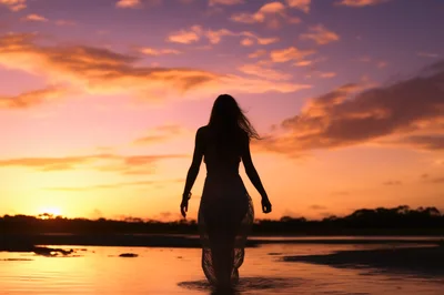 Silhouette Of A Woman Walking Through Shallow Water At Sunset