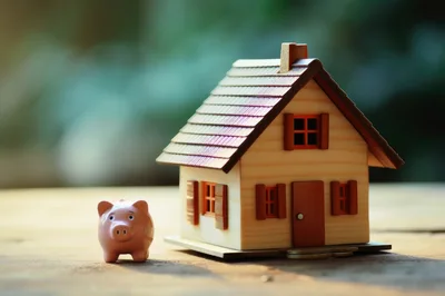 Miniature House Model And Piggy Bank On Wooden Table