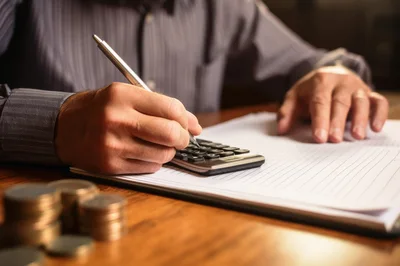 Businessman Calculating Finances With Coins On Desk