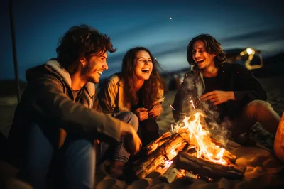 Friends Laughing Around A Beach Bonfire At Night
