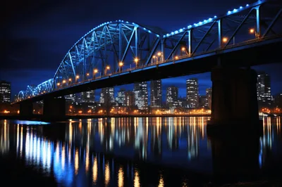 Illuminated Steel Truss Bridge Over City River At Night