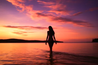Silhouette Of A Woman Walking In The Ocean At Sunset