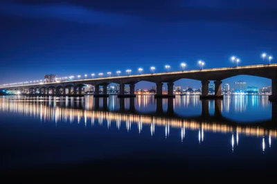 Illuminated Bridge Over Calm Water At Night