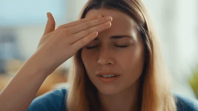 Stressed Woman Rubbing Her Forehead In Indoor Setting