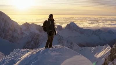 Mountaineer Standing On Snowy Mountain Peak At Sunset