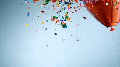 Red Balloon Exploding With Colorful Confetti Against Blue Background