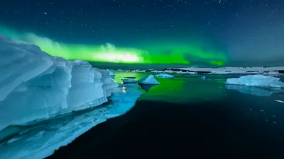 Aurora Borealis Shimmering Over Arctic Icebergs In Still Water