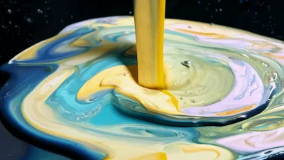 Yellow Paint Pouring Into Colorful Swirling Liquid Mixture