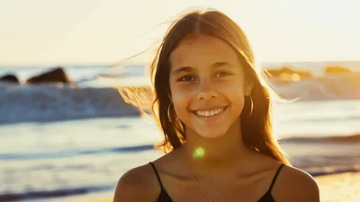 Smiling Young Girl Standing On Beach At Sunset