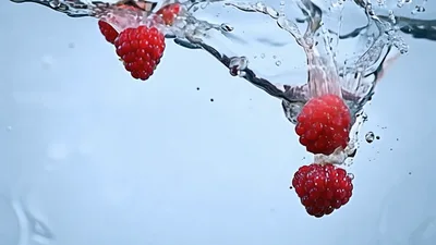 Fresh Raspberries Falling Into Clear Water With Splashes
