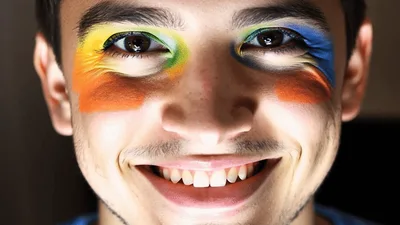 Young Man With Rainbow Face Paint Smiling At Camera