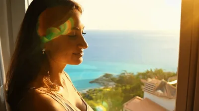 Woman Opening Curtains To Reveal Beautiful Tropical Ocean View