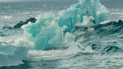 Blue Iceberg Floating In Ocean And Distant Field Explosions