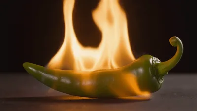 Green Chili Pepper Engulfed In Bright Orange Flames