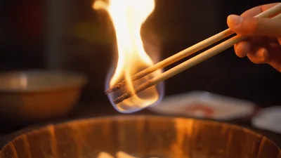 Burning Wooden Chopsticks Held Over A Wooden Bowl