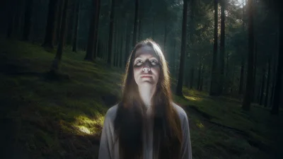Young Woman Standing In A Dark Forest Looking Up