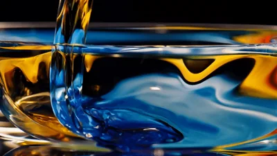 Yellow Liquid Pouring Into Blue Liquid In Glass Bowl