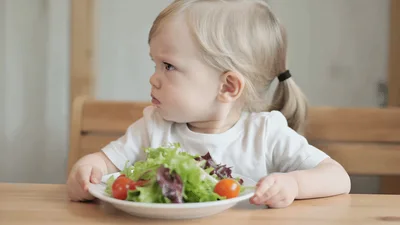 Toddler Sitting At Table Looking Unhappy With Salad