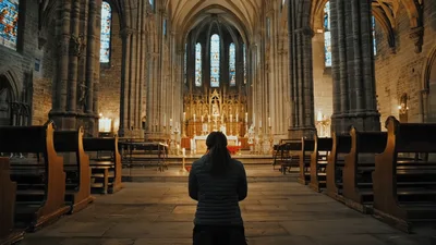 Woman Kneeling In Prayer Inside A Gothic Cathedral